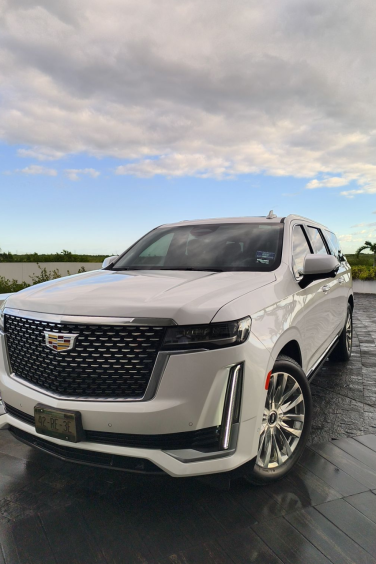 A white Cadillac SUV is parked on a driveway under a partly cloudy sky, special for cancun luxury transportation